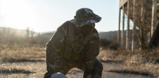 A soldier in tactical gear apprehending a person on the ground in an outdoor setting