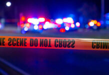 Caution tape at a crime scene with police lights in the background